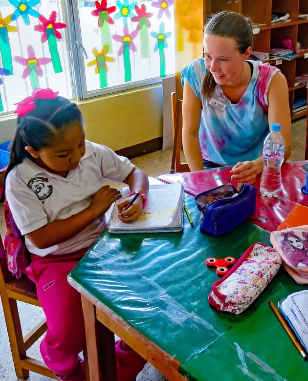 A student in a study abroad program in Mexico sits with an elementary school student in a classroom